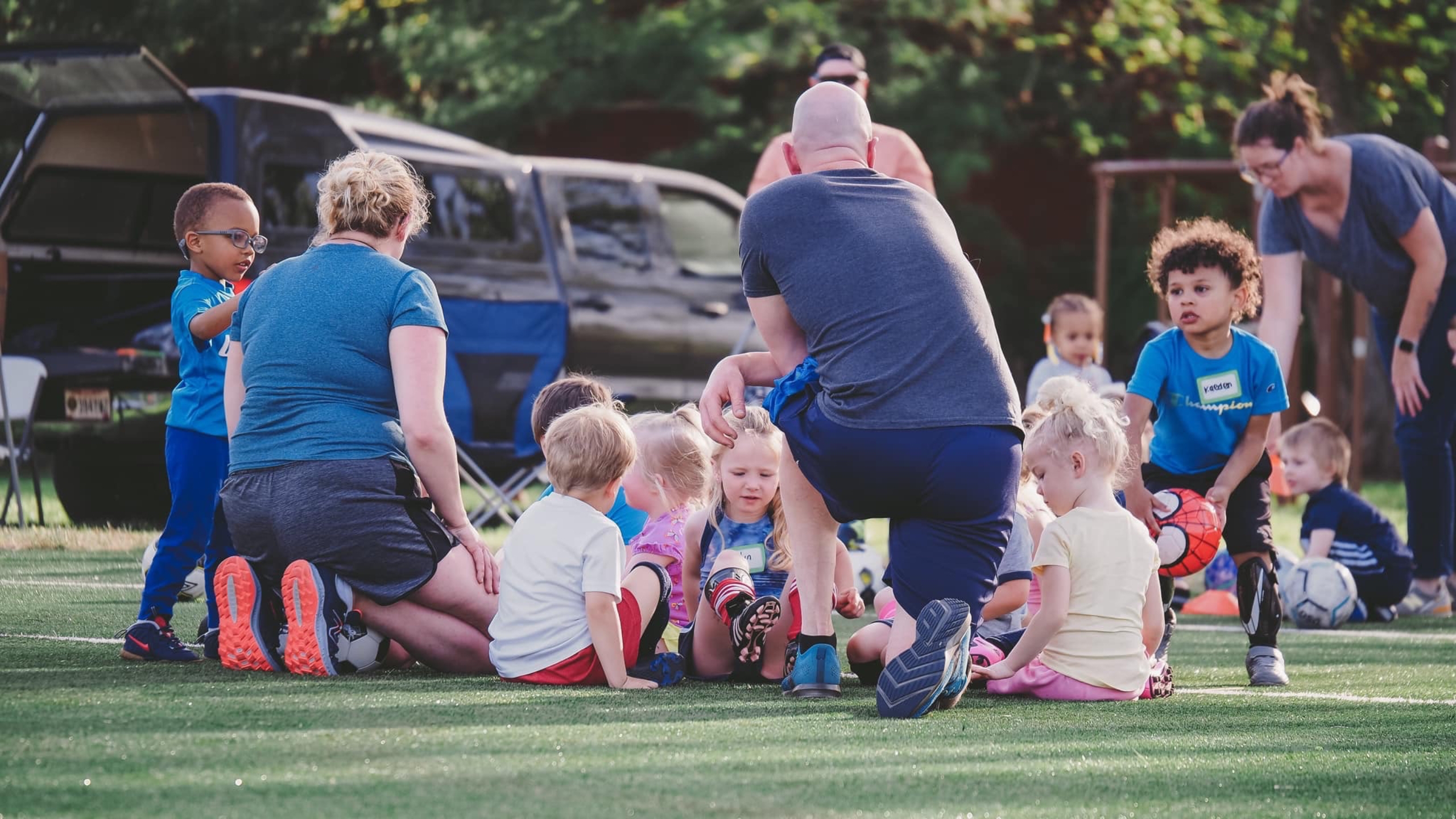 A group of children sitting on the grass in front of a car.